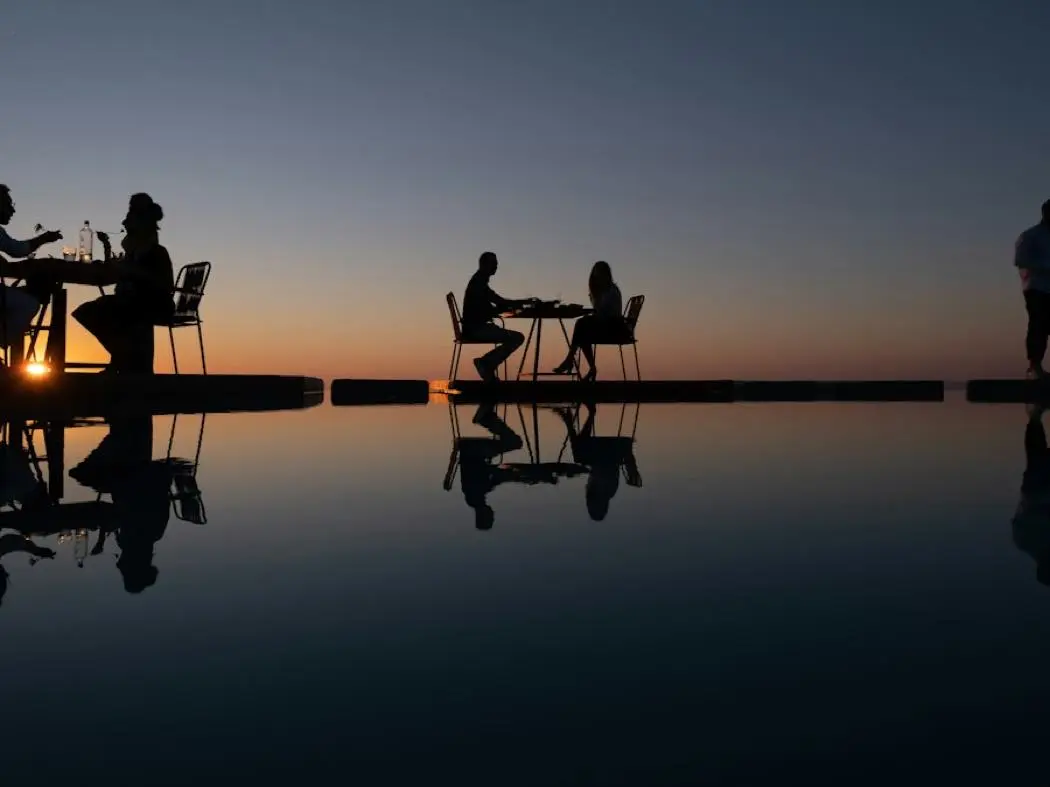 Travellers dining at tables on the water at sunset