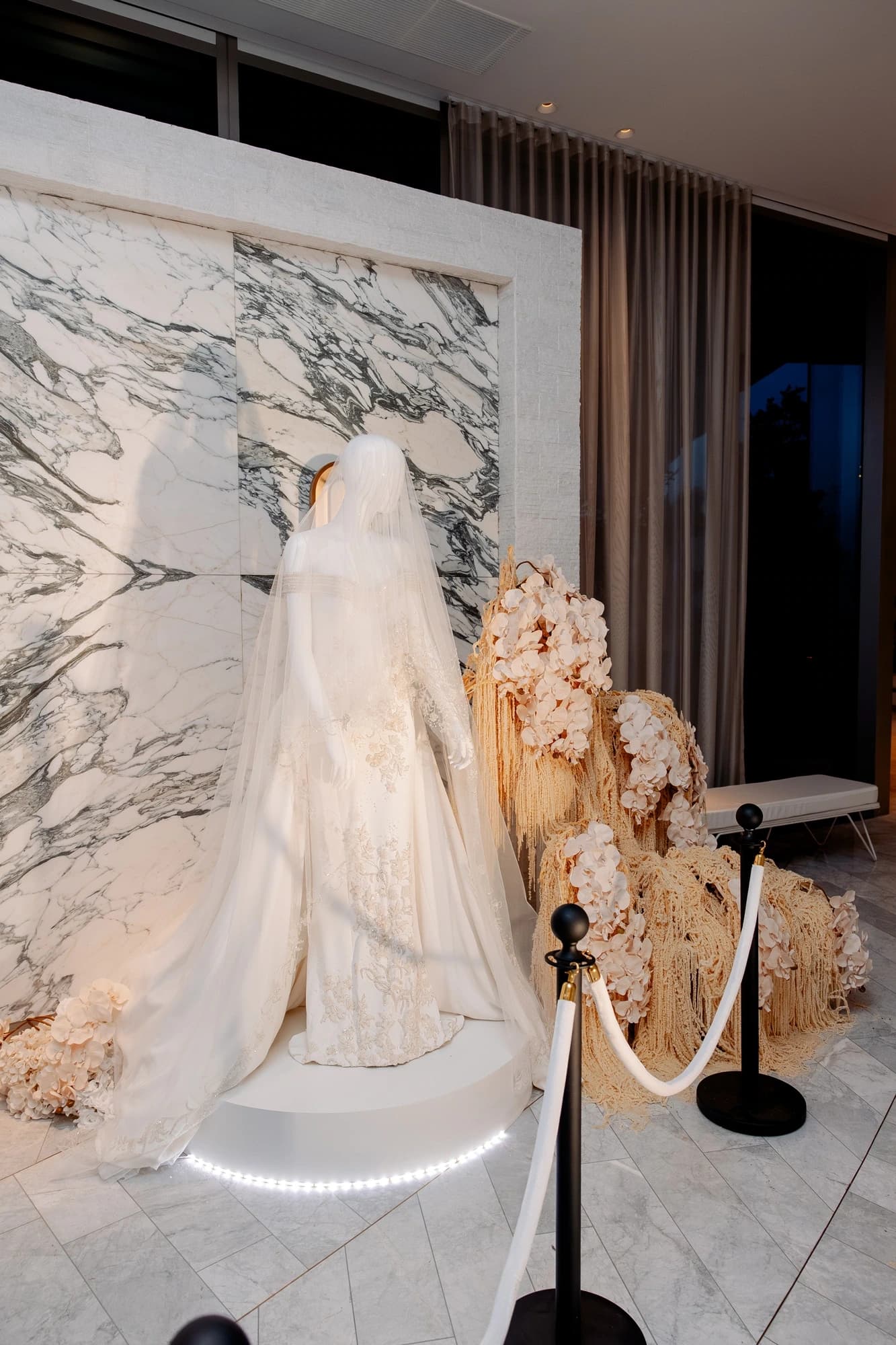 A couture gown displayed on a lit plinth beside a floral installation at Wedded World
