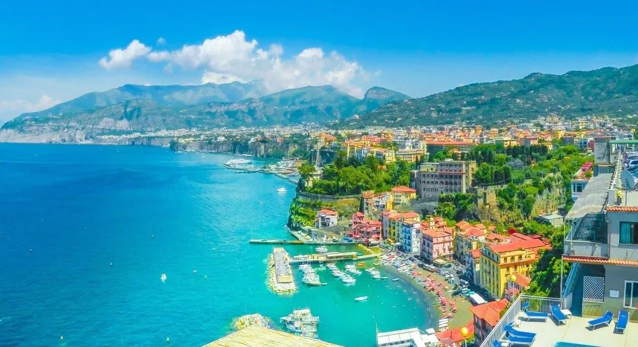 Sorrento and its harbour above turquoise water, with mountains beyond