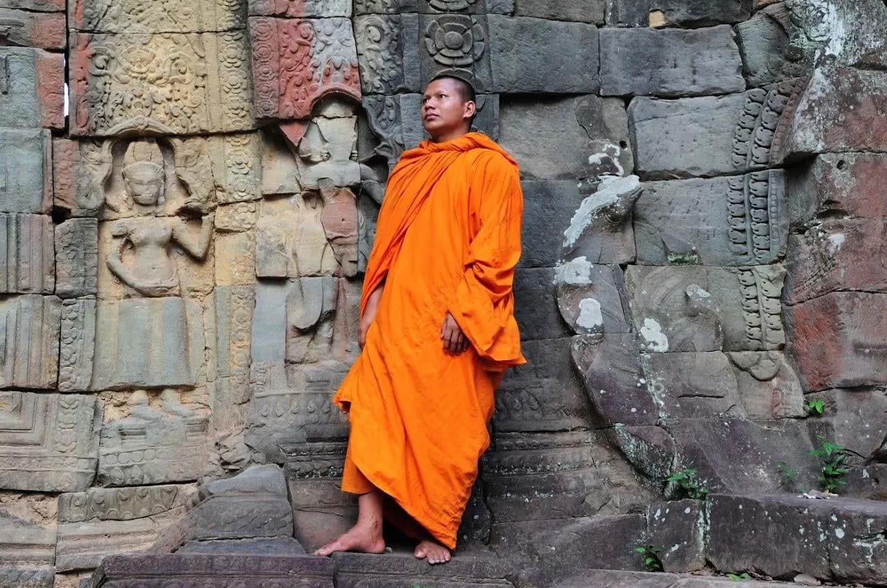 A monk in saffron robes standing against a carved temple wall