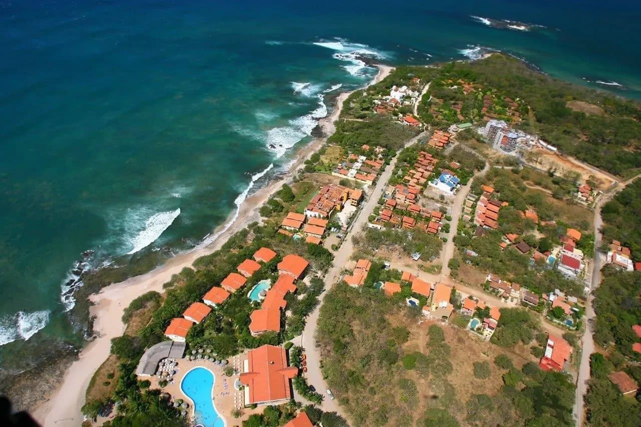 Aerial view of red-roofed houses and a pool beside a rocky Pacific shore