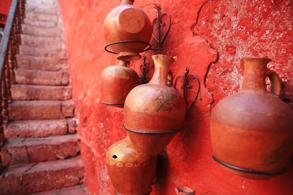 Clay water jugs hanging on a red wall beside stone steps