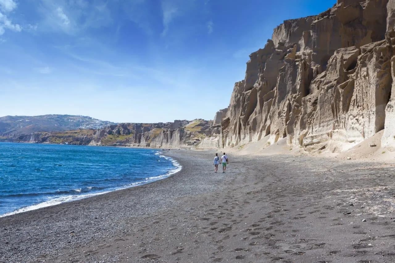 A dark sand beach below pale cliffs on Santorini
