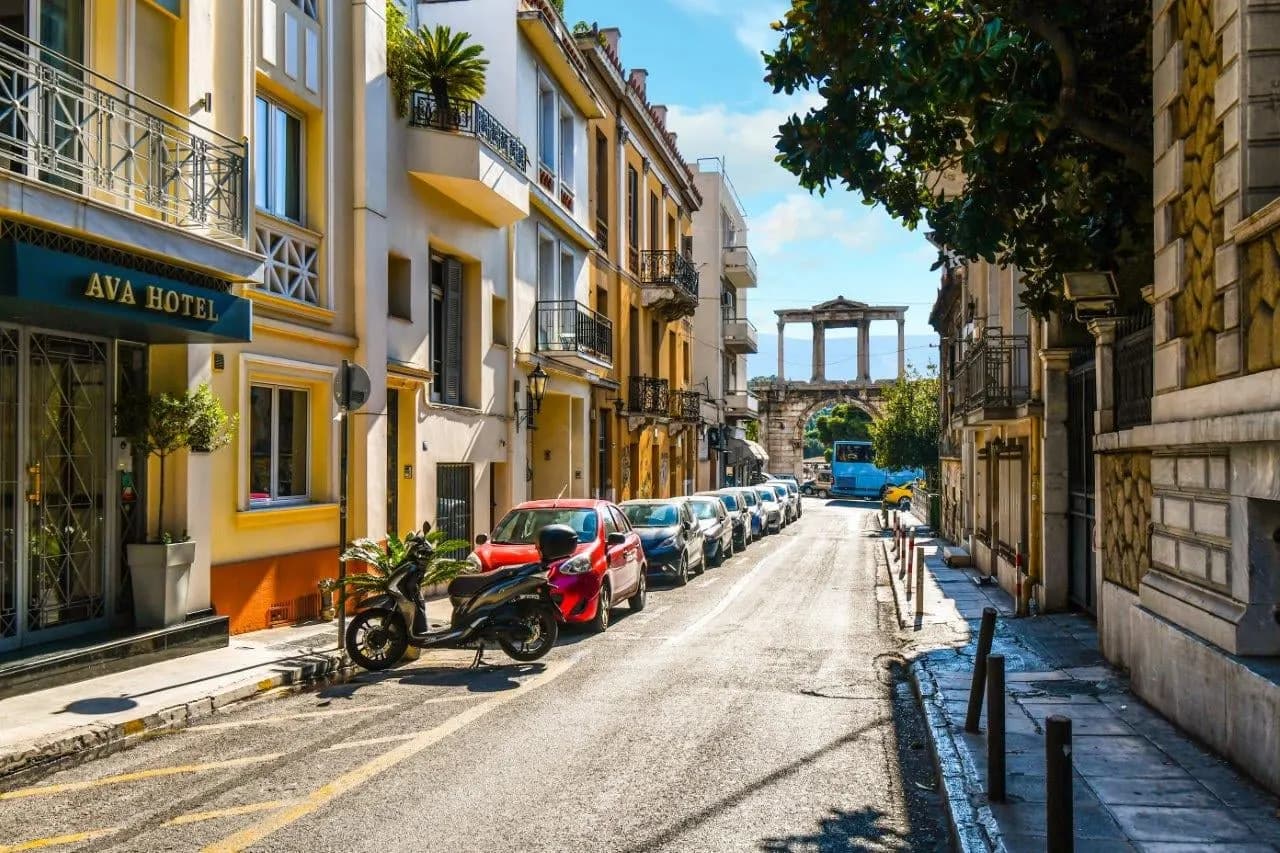 A quiet Athens street of neoclassical buildings leading to an ancient arch