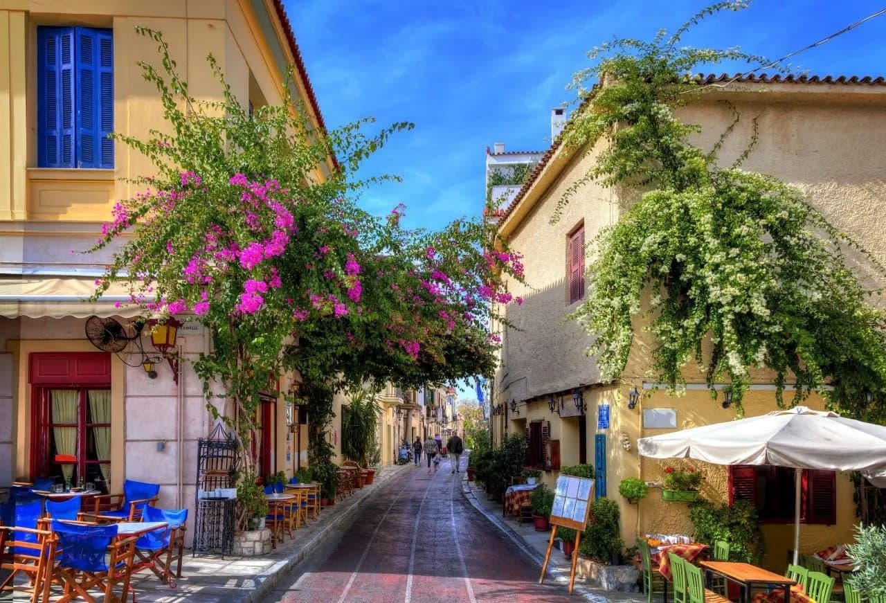 A Plaka street with pink bougainvillea over cafe tables and old houses