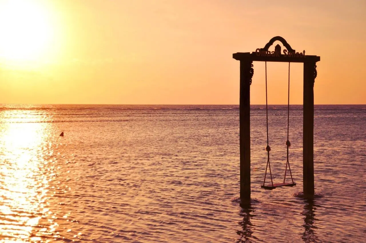 A wooden swing standing in the shallows off Gili Trawangan at sunset