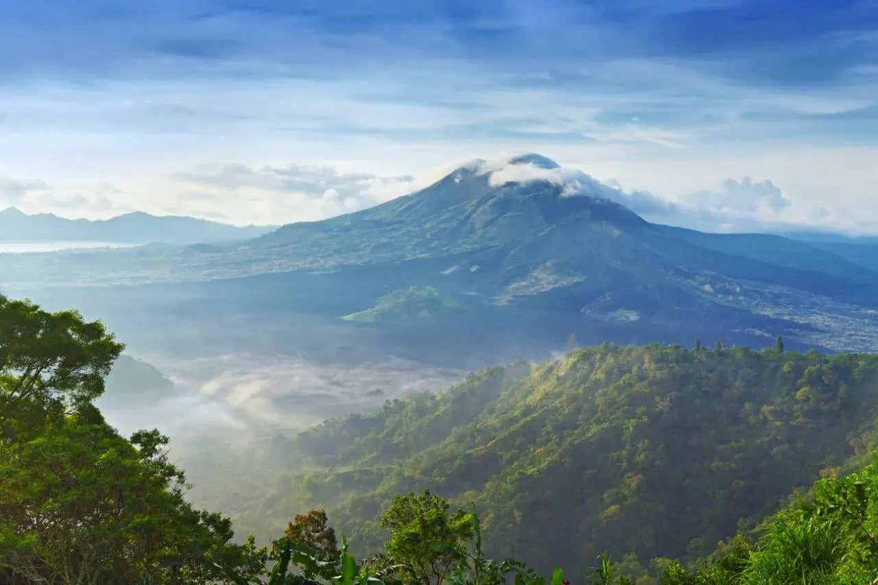 Mount Batur rising above misty green valleys in the morning