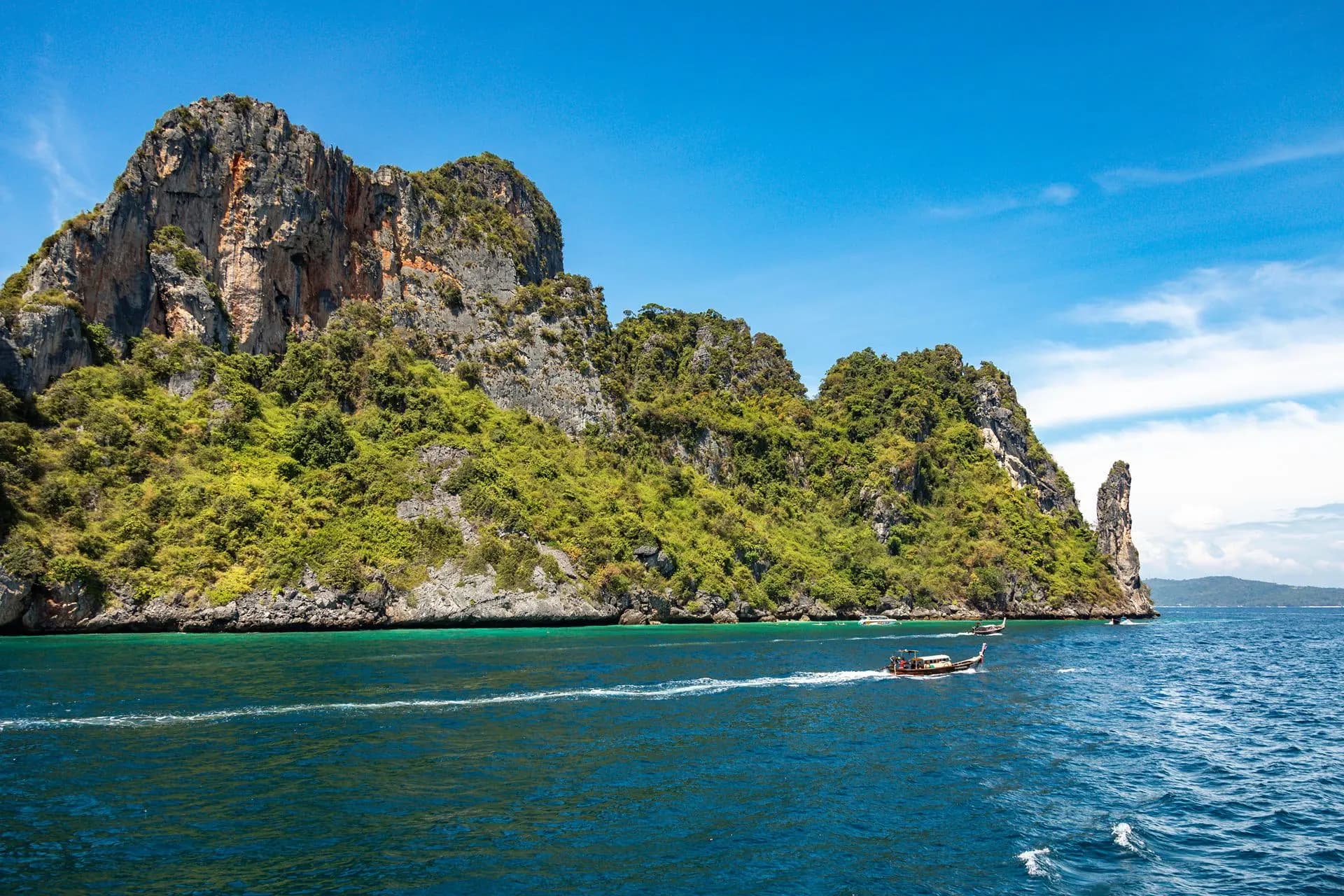 A speedboat passing a green limestone island in the Andaman Sea