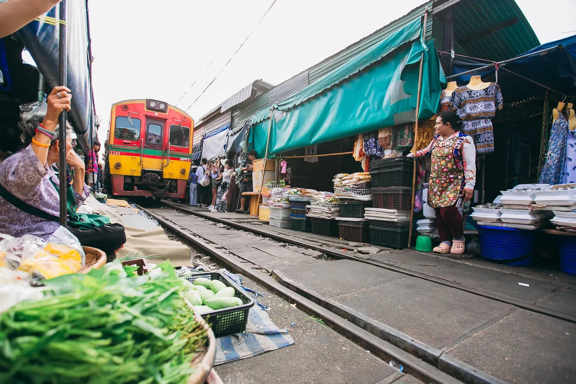 A train approaching between market stalls and produce on the tracks at Maeklong