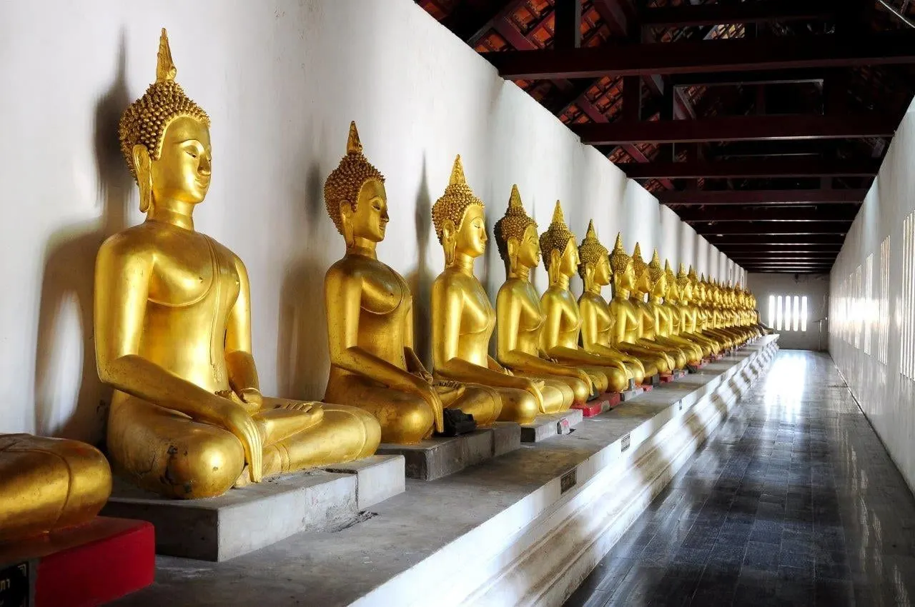 A long row of golden seated Buddhas in a temple gallery
