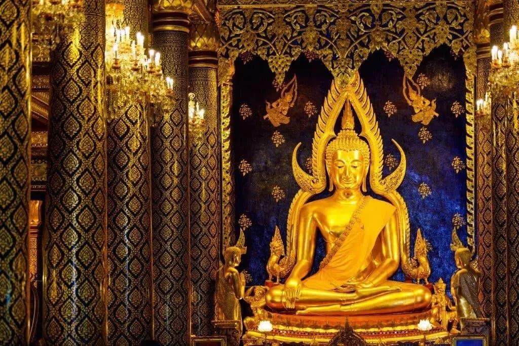 A golden seated Buddha framed by an ornate halo inside a temple hall