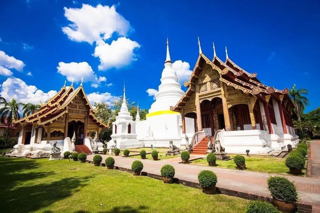 Teak temple halls and a white chedi in Chiang Mai under a blue sky