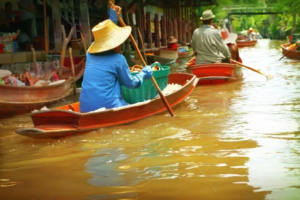 Vendors in woven hats paddling wooden boats along a market canal