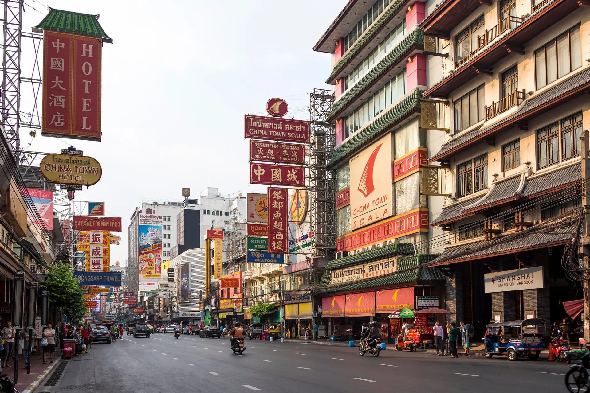Shopfronts and hanging signs along a busy Chinatown road in Bangkok