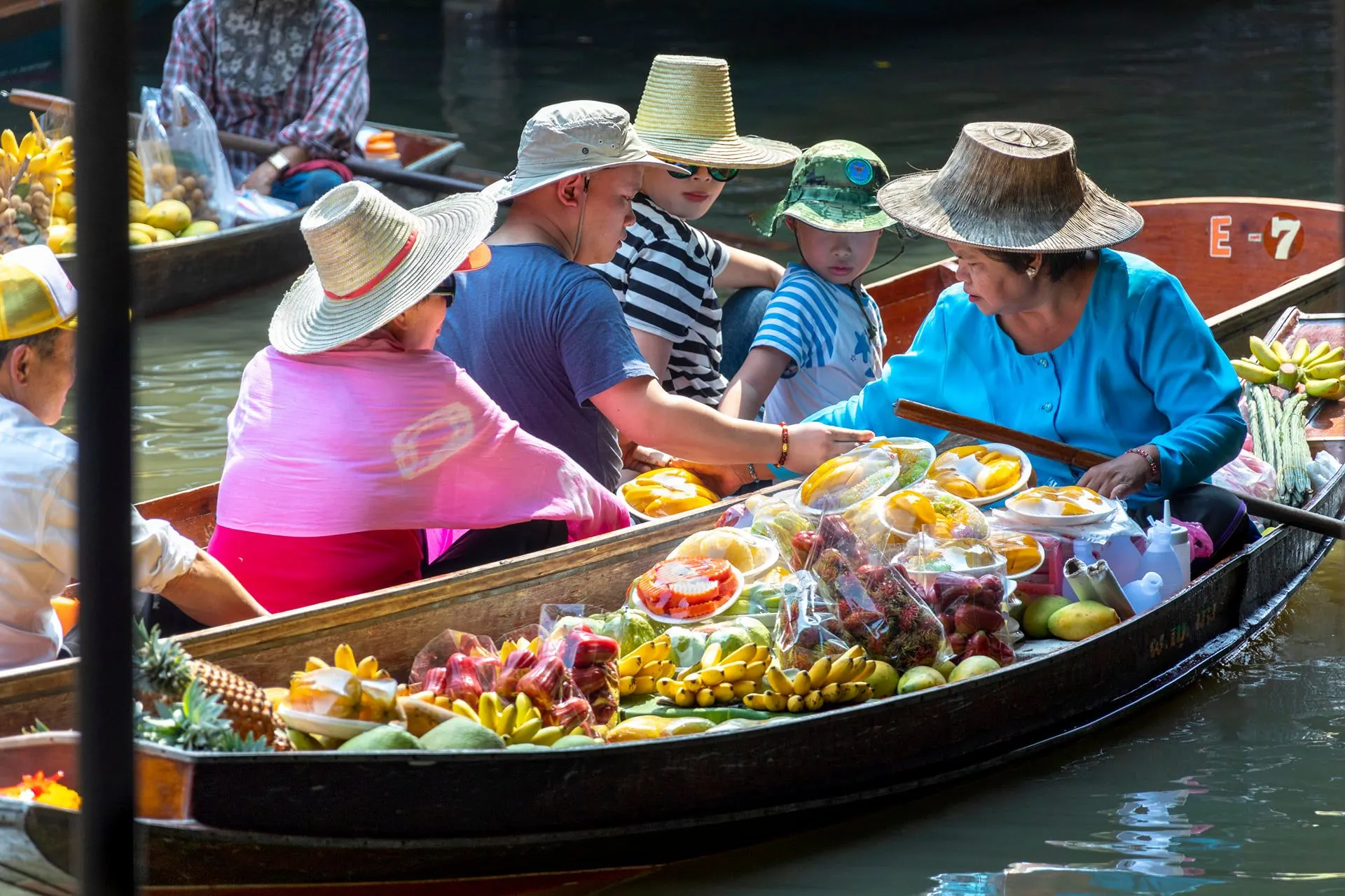 Visitors in sun hats beside a boat piled with fruit at a floating market