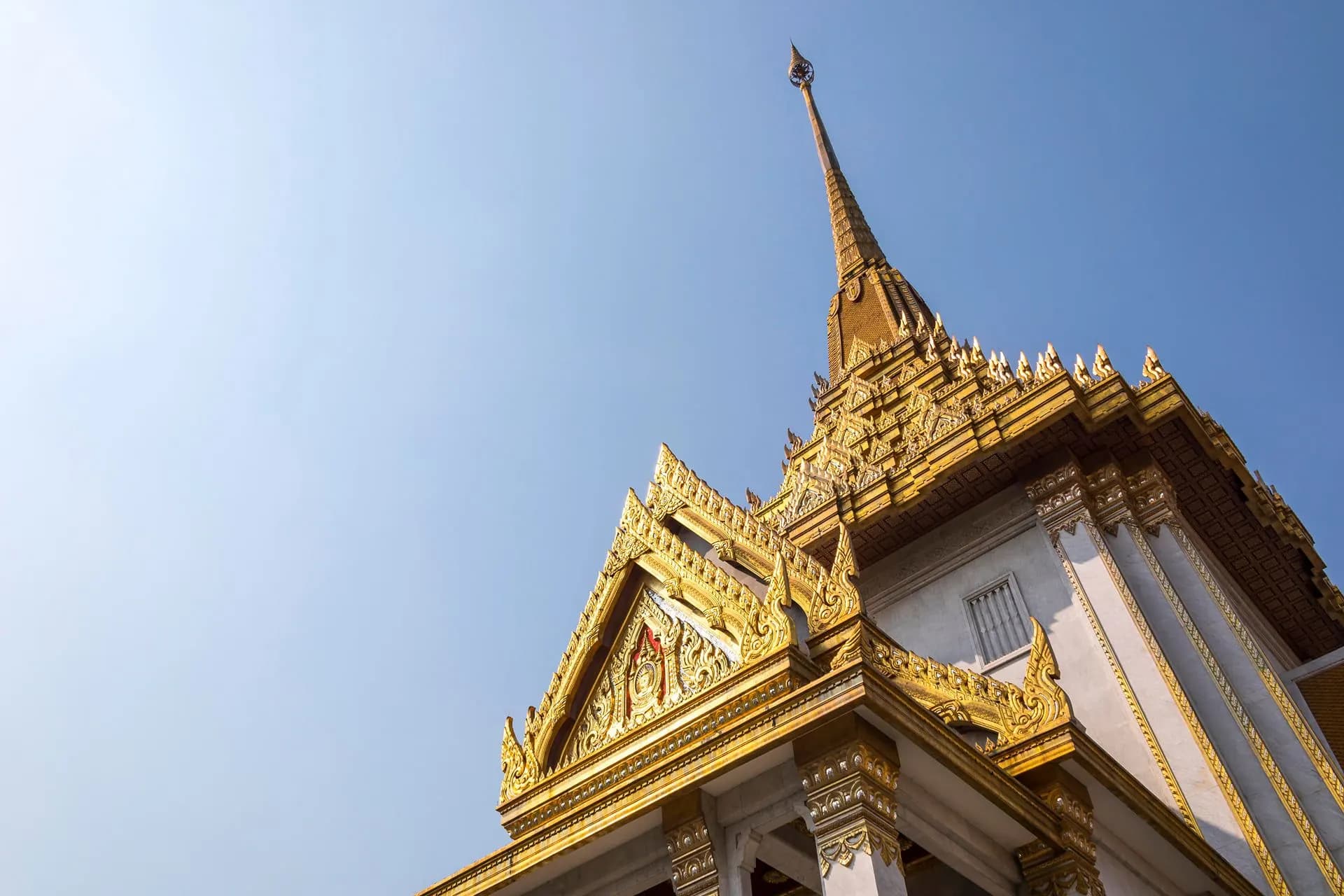 The gilded roof and spire of Wat Traimit against a blue sky