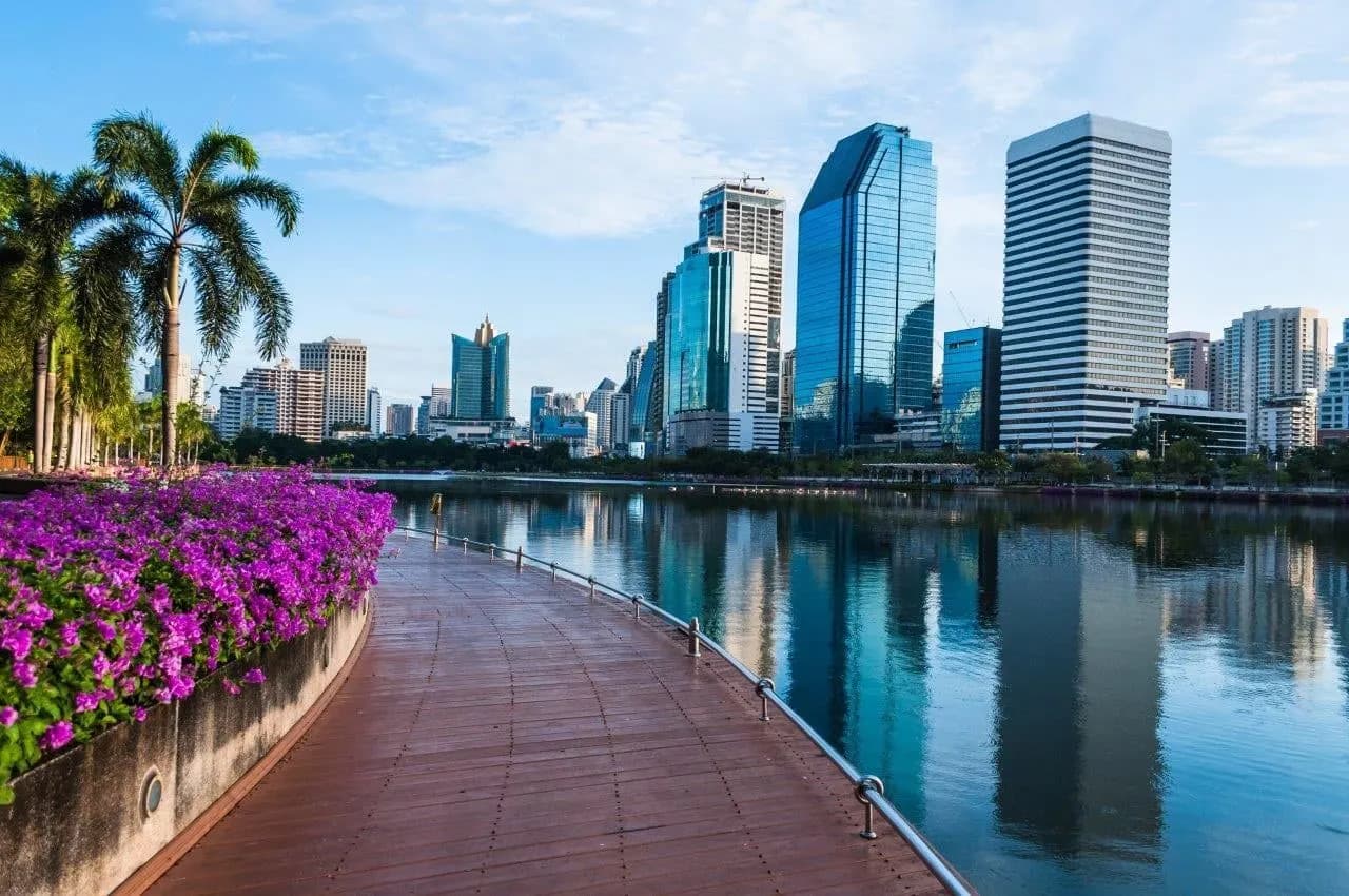A lakeside walkway with bougainvillea and city towers reflected in the water