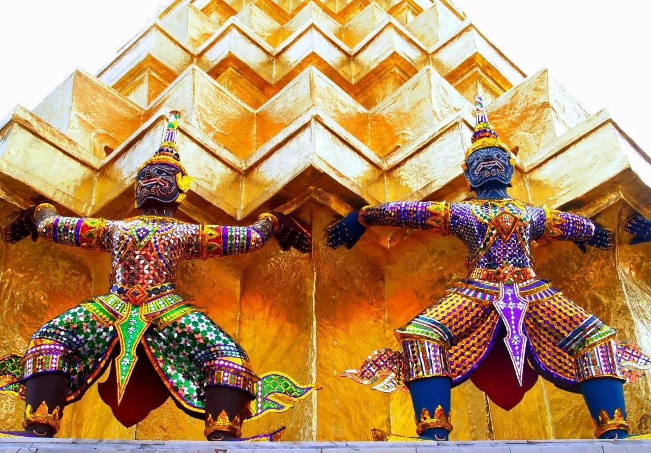 Painted demon figures supporting a golden chedi at the Grand Palace