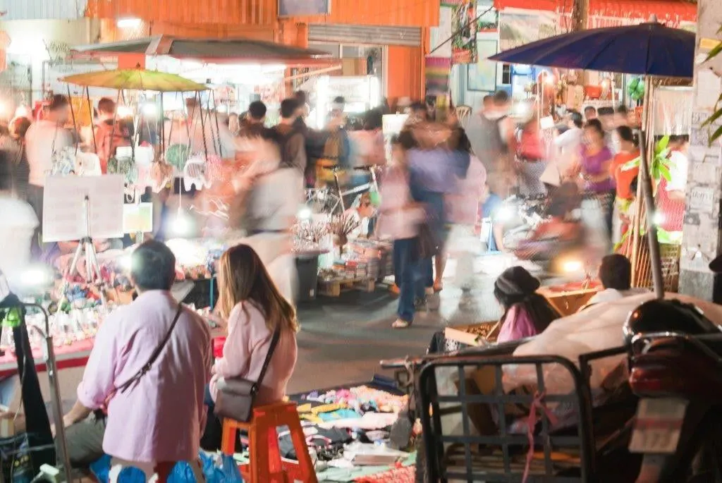 Shoppers at a busy evening market lit by stall lamps