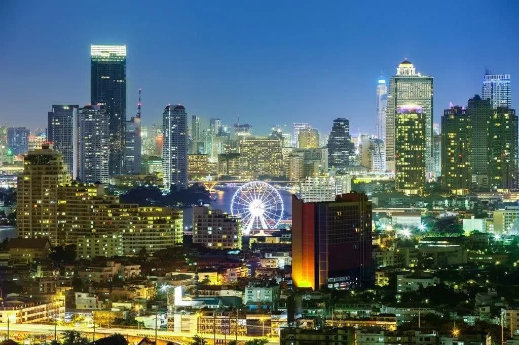 City towers and a lit Ferris wheel by the river at night