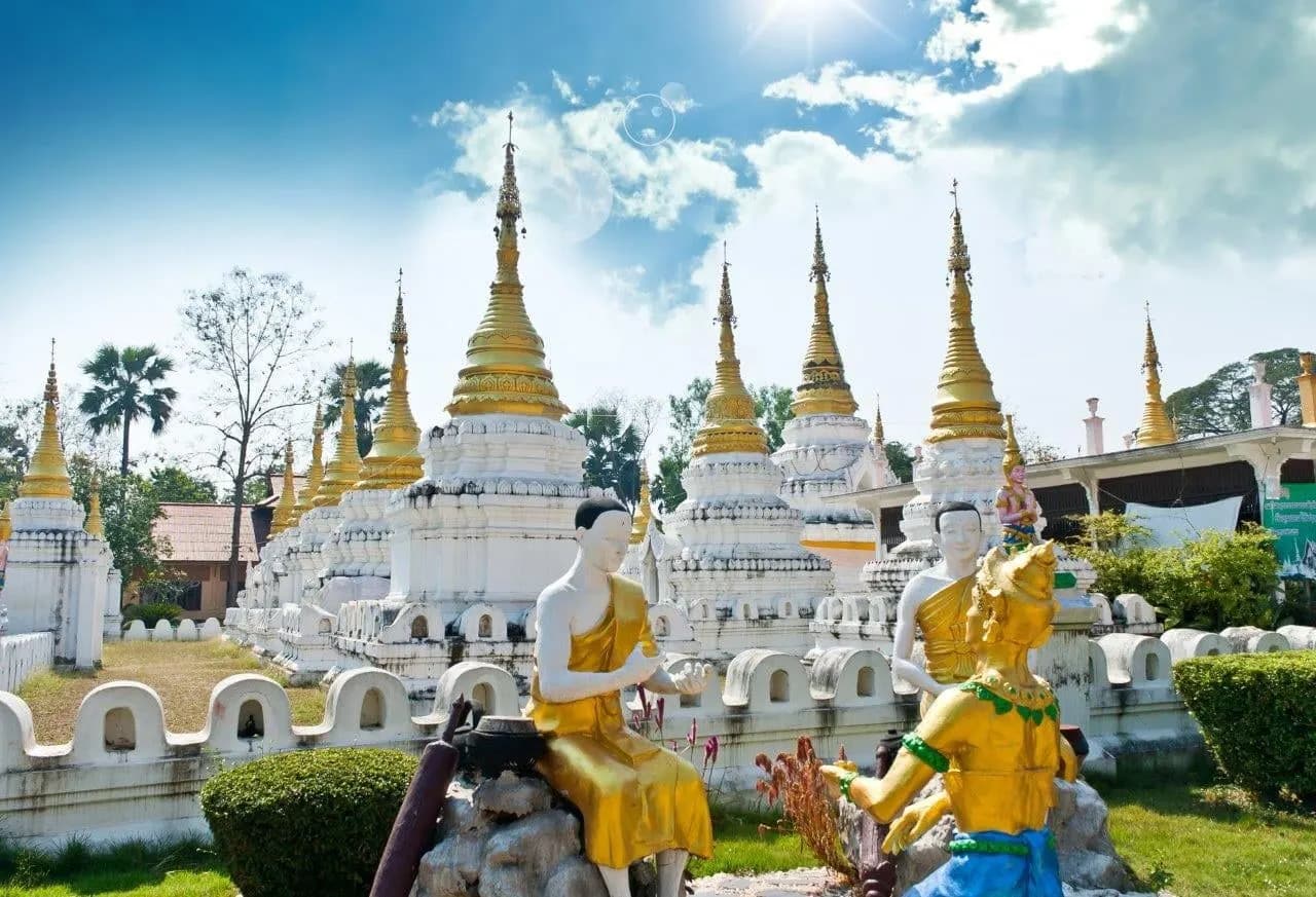 Rows of white and gold chedis behind painted guardian statues