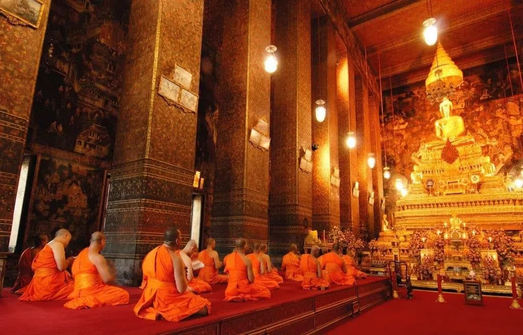 Monks in saffron robes seated before a golden Buddha in a temple hall