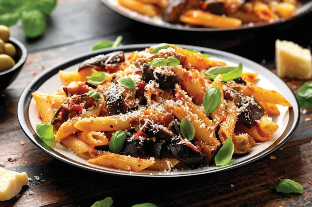 A plate of pasta with aubergine, tomato, basil and grated cheese