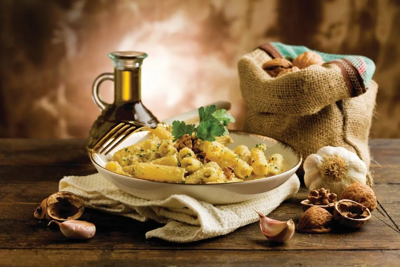 Pasta with walnuts and parsley beside a bottle of olive oil and a sack of nuts