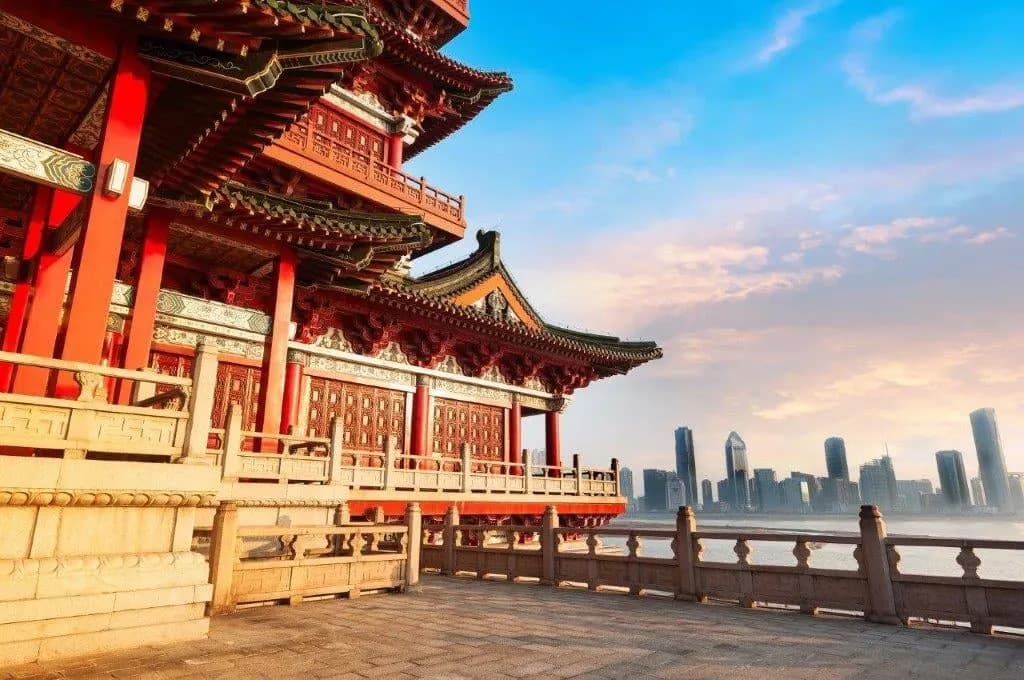 A red-columned pavilion with a modern skyline in the distance