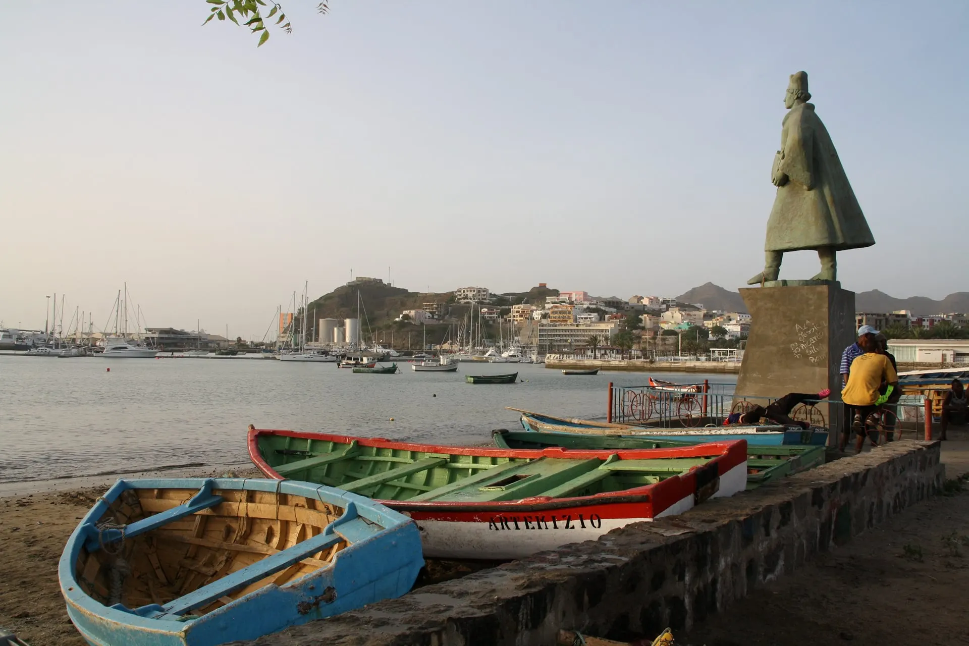 Painted fishing boats beside a bronze statue on a harbour front