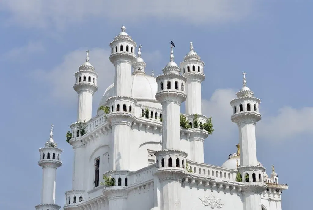 A white mosque with many slender minarets against a blue sky