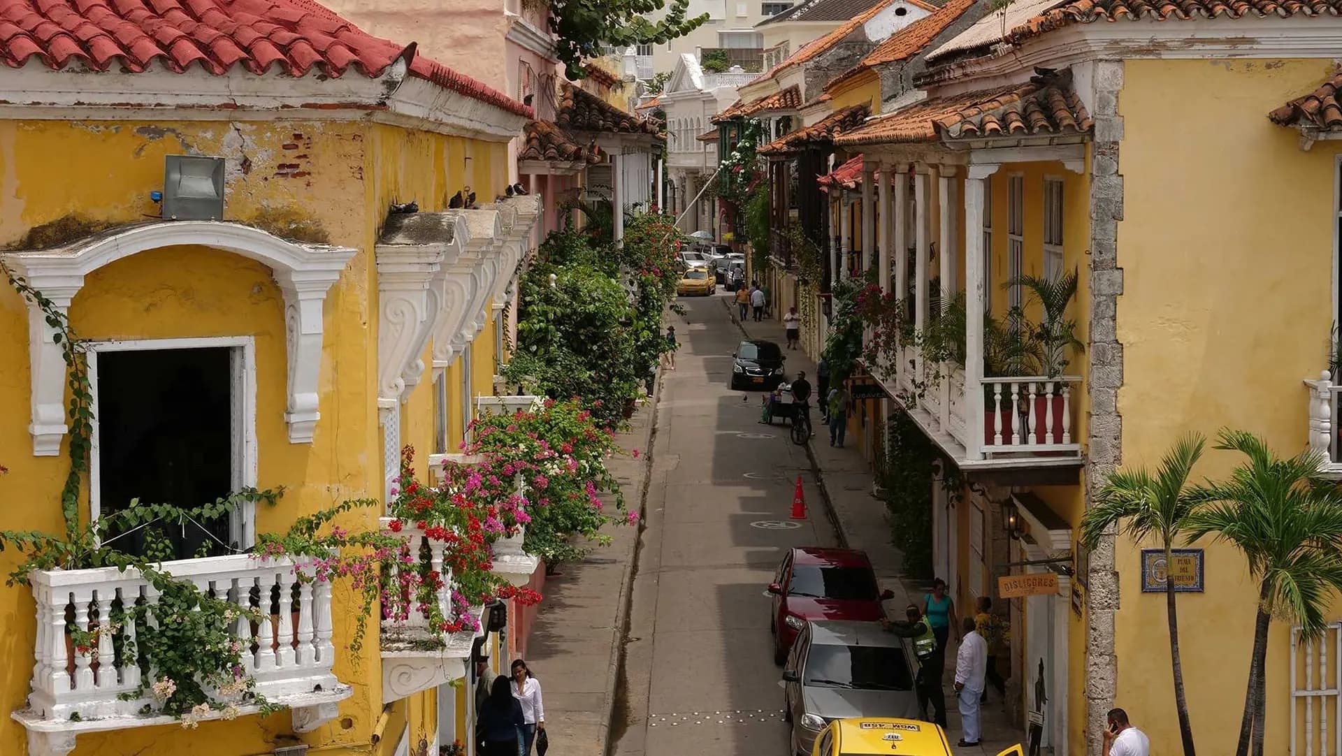 A narrow street of yellow colonial houses with white balconies and palms