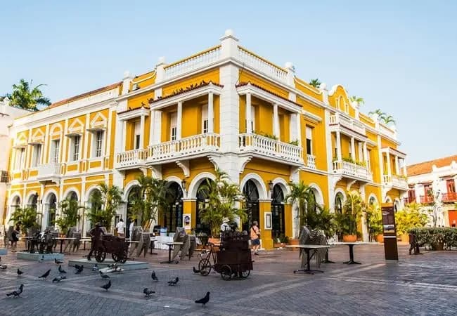 A yellow colonial building with arcades on a plaza in late afternoon light