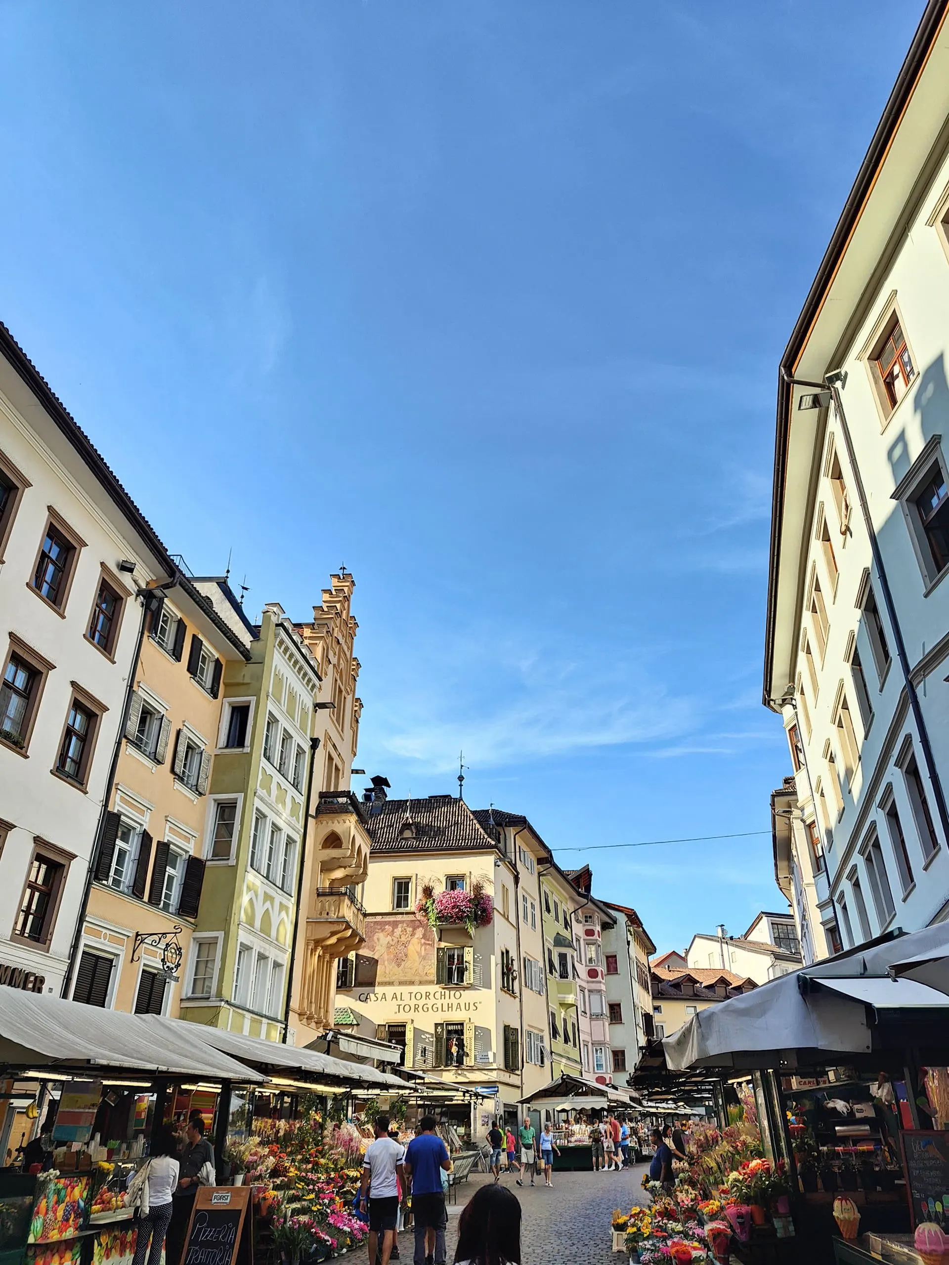 Market stalls of fruit and flowers along a street of painted houses in Bolzano