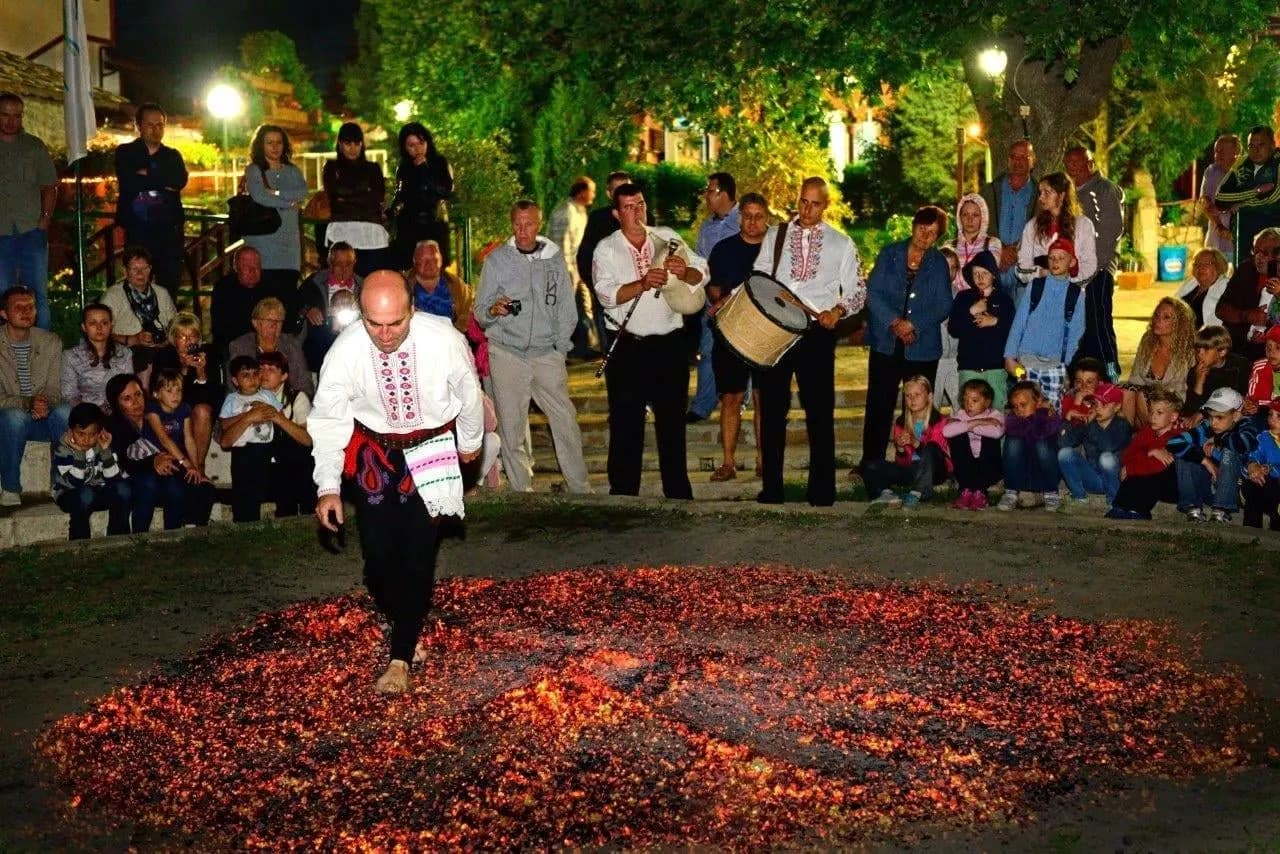 A dancer in folk costume crossing glowing embers as a crowd looks on