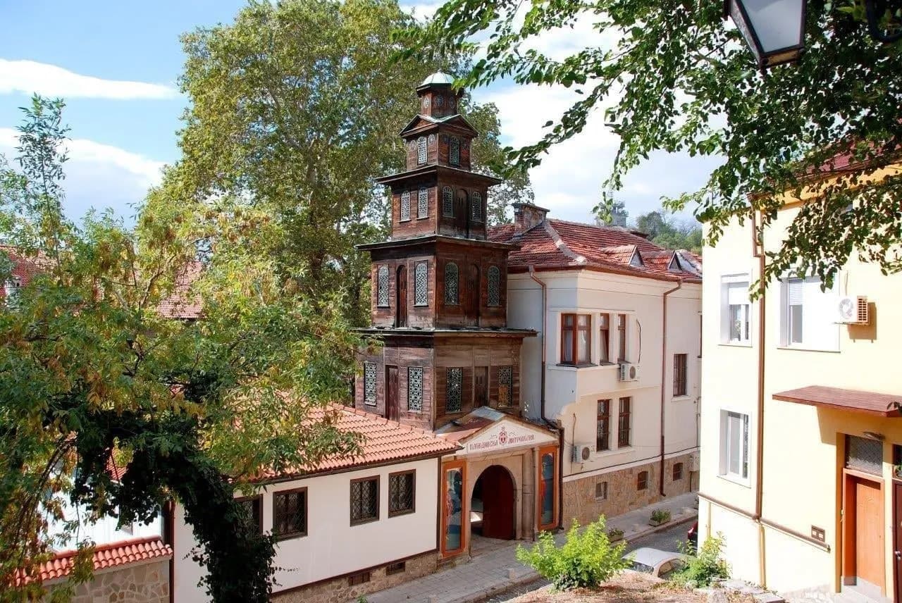 A Revival-era house with a wooden tower among trees in an old town