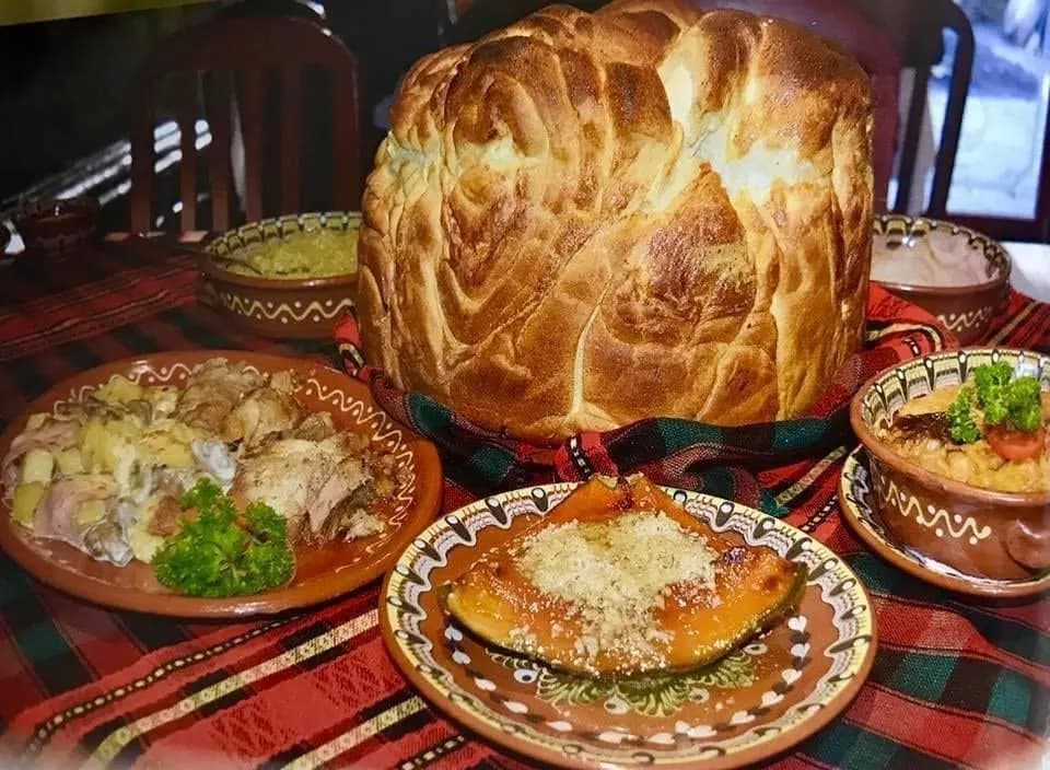 A round loaf of braided bread among clay dishes of Bulgarian food