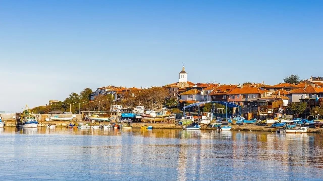 An old seaside town with a church tower above a calm harbour of small boats