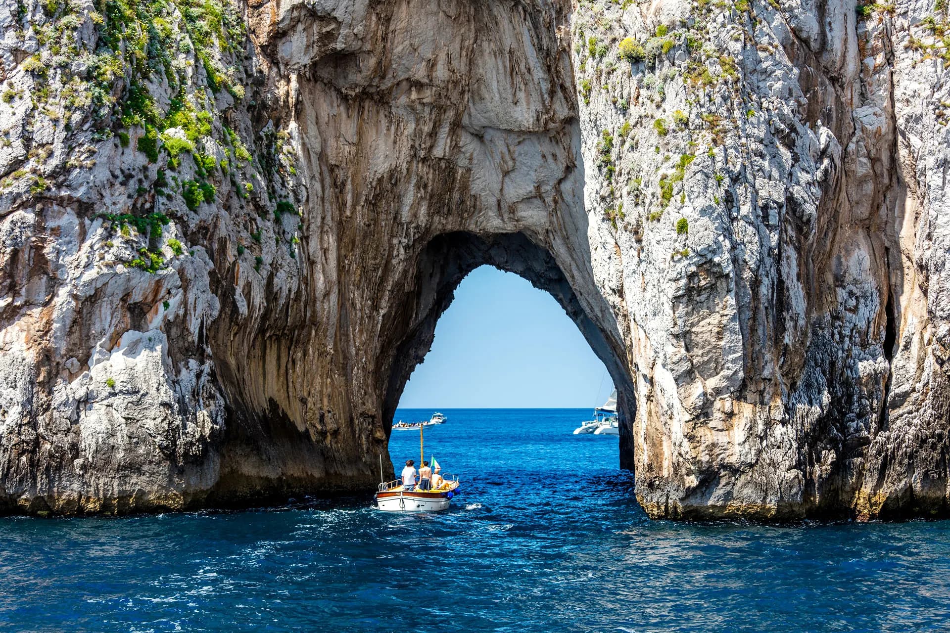 A small boat passing through a natural rock arch off Capri