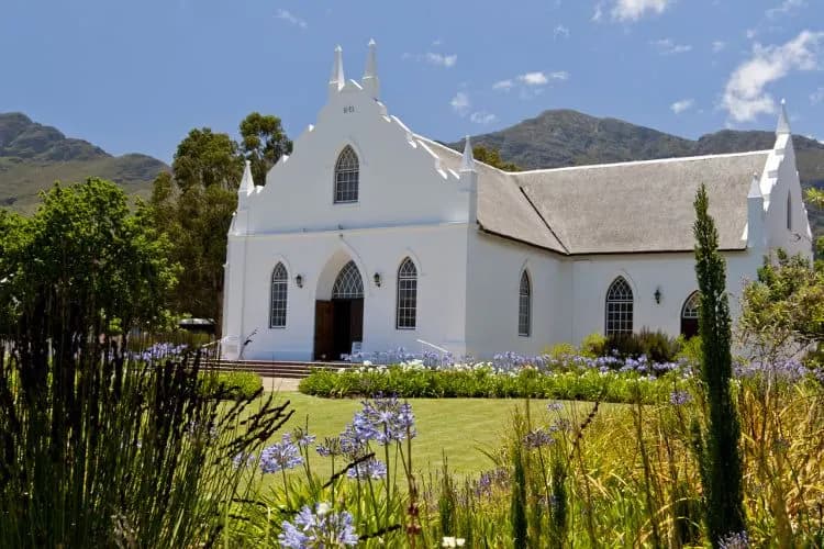 A white gabled church among gardens below the mountains
