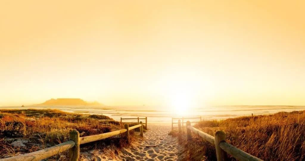 A sandy boardwalk to the beach, with Table Mountain across the bay in golden light