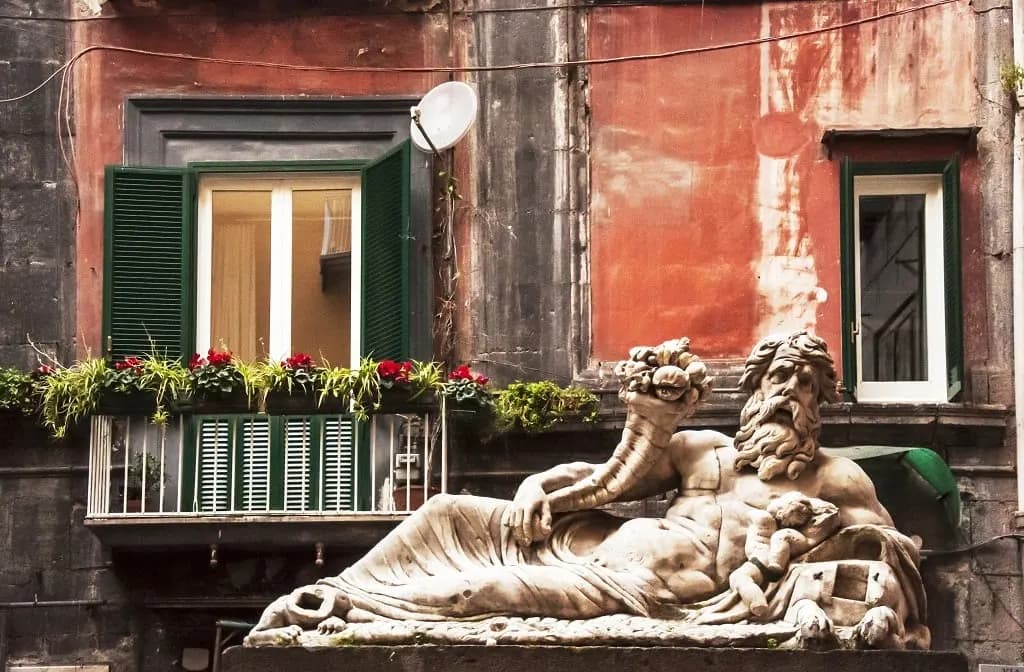 A reclining marble statue before a weathered red façade in the old centre of Naples