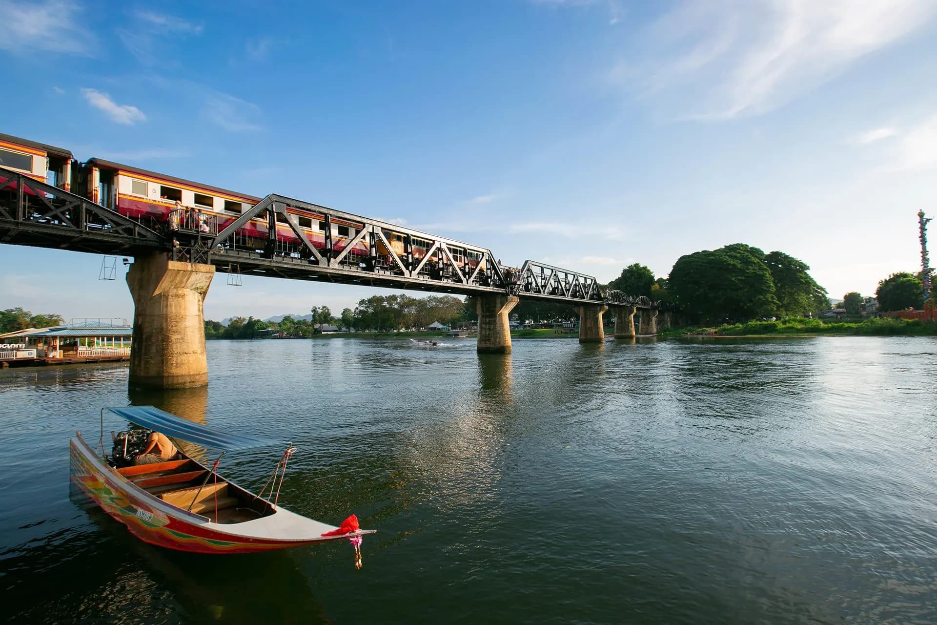 A train crossing the iron bridge over the River Kwai, with a boat moored below