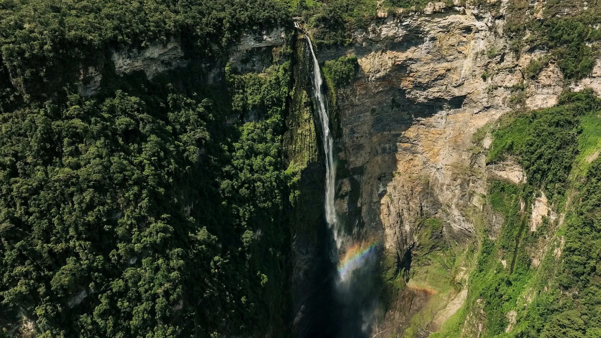 Gocta waterfall falling past a cliff with a rainbow in its spray