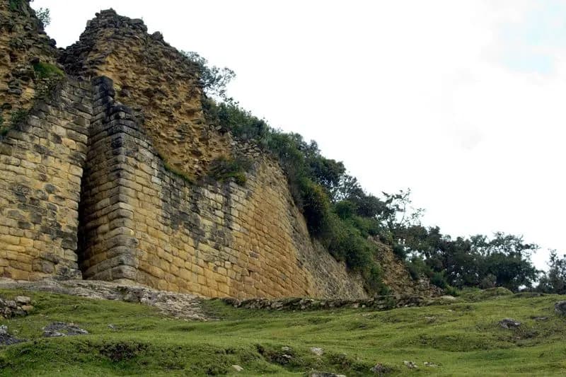 The high limestone outer wall of the Kuélap citadel above a grassy slope