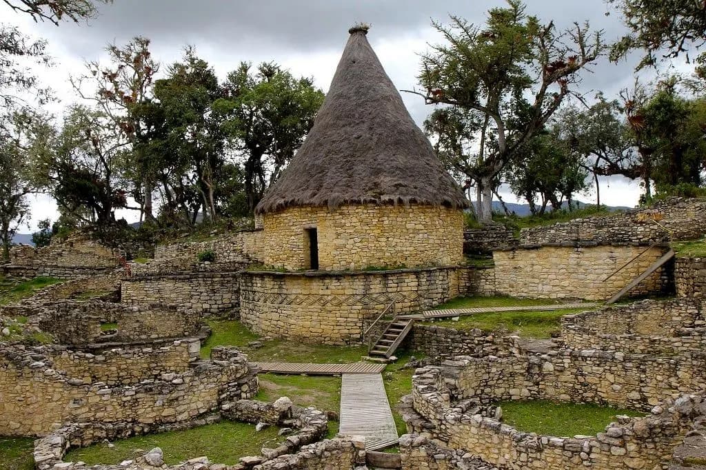 A rebuilt round stone house with a tall conical thatched roof inside Kuélap
