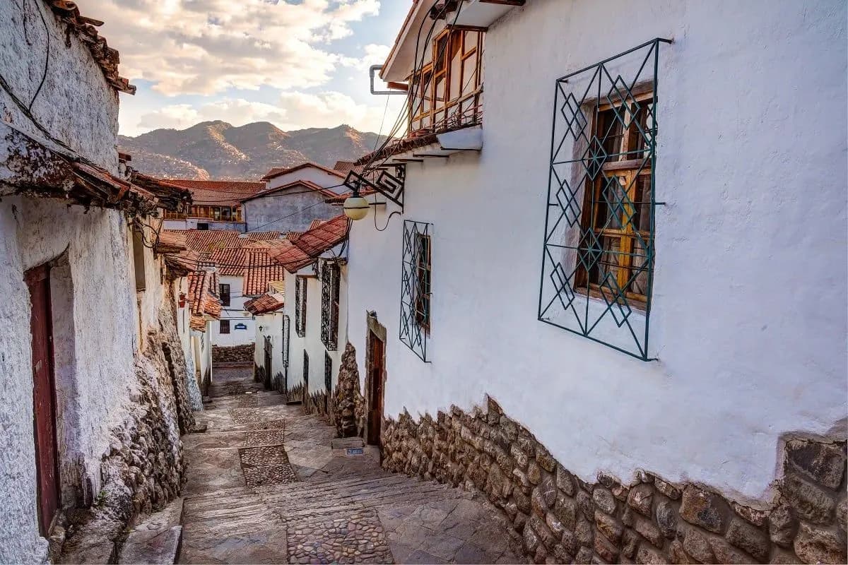 A cobbled lane between white walls in Cusco, with mountains beyond