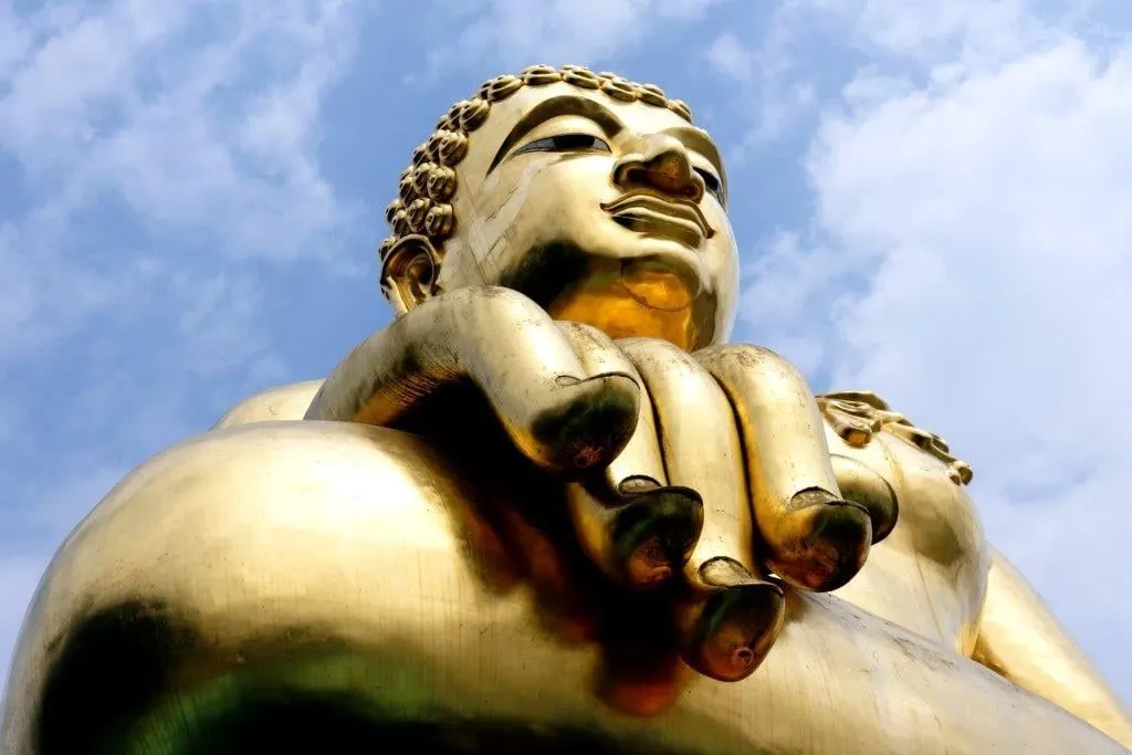 A giant golden Buddha against a blue sky with clouds