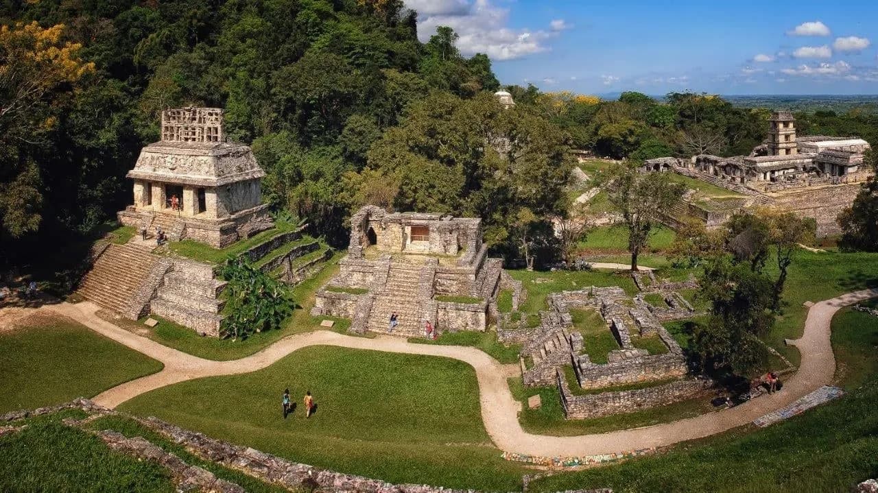 Temples with carved roof combs on the lawns of Palenque, with the palace tower beyond
