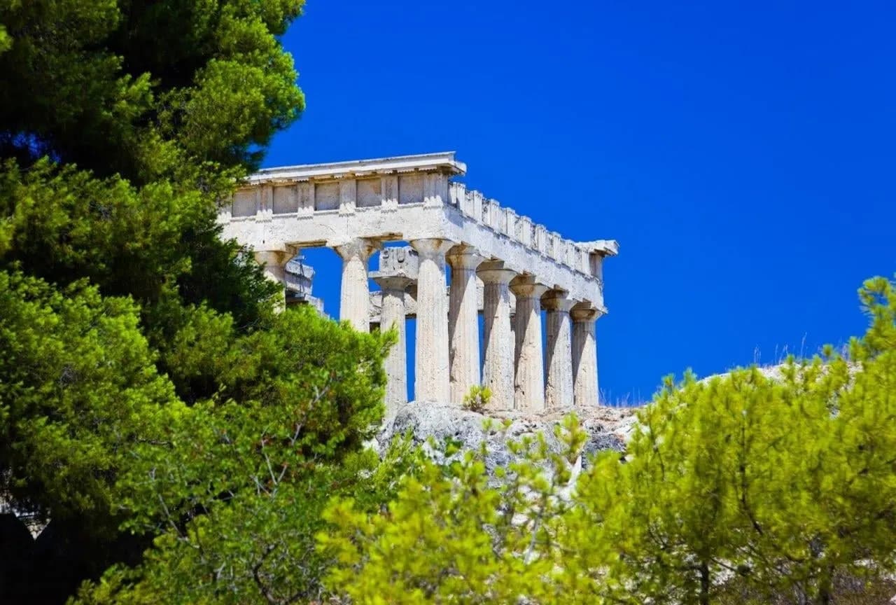 A Doric temple framed by pine trees under a deep blue sky